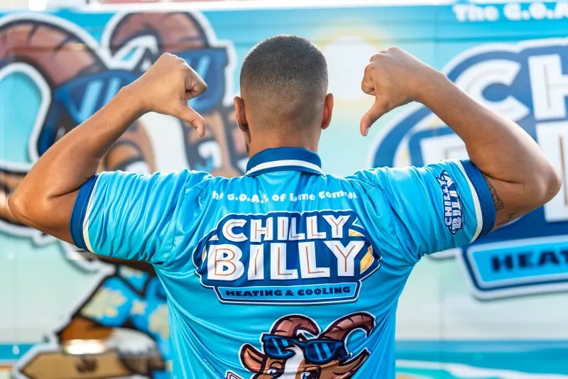 A Chilly Billy technician seen from behind, pointing to the Chilly Billy Heating & Cooling logo on his uniform in front of the wrapped van