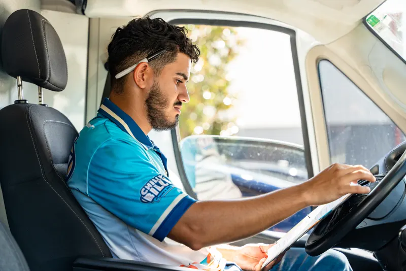 A Chilly Billy technician in the driver's seat of a service van checking the route with a pencil behind his ear