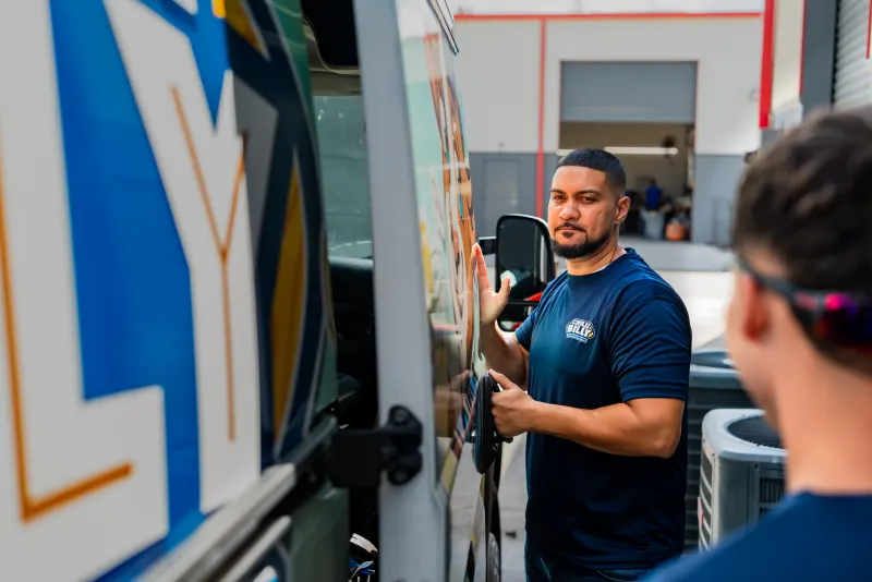 A Chilly Billy technician opening the door of the wrapped service van at the shop, a condenser unit visible behind him