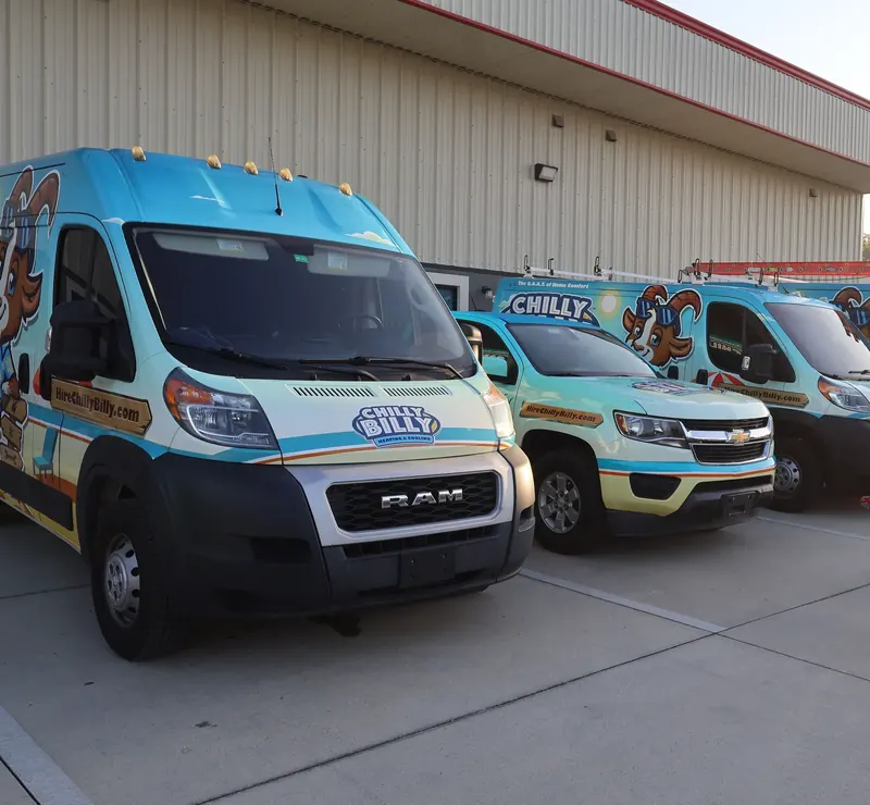 Chilly Billy wrapped service vans and a pickup truck parked in a row outside a metal-sided building