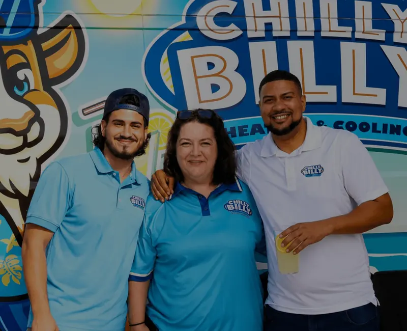 Three people in Chilly Billy polos smiling in front of the company van wrap, one holding a yellow drink