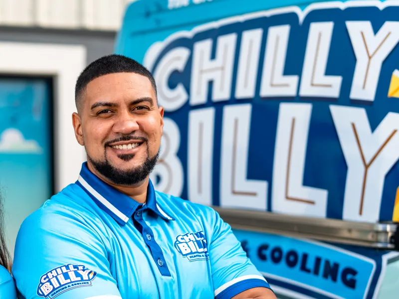 Chris Javier, owner and license holder of Chilly Billy Heating & Cooling, in a company polo in front of the wrapped service van